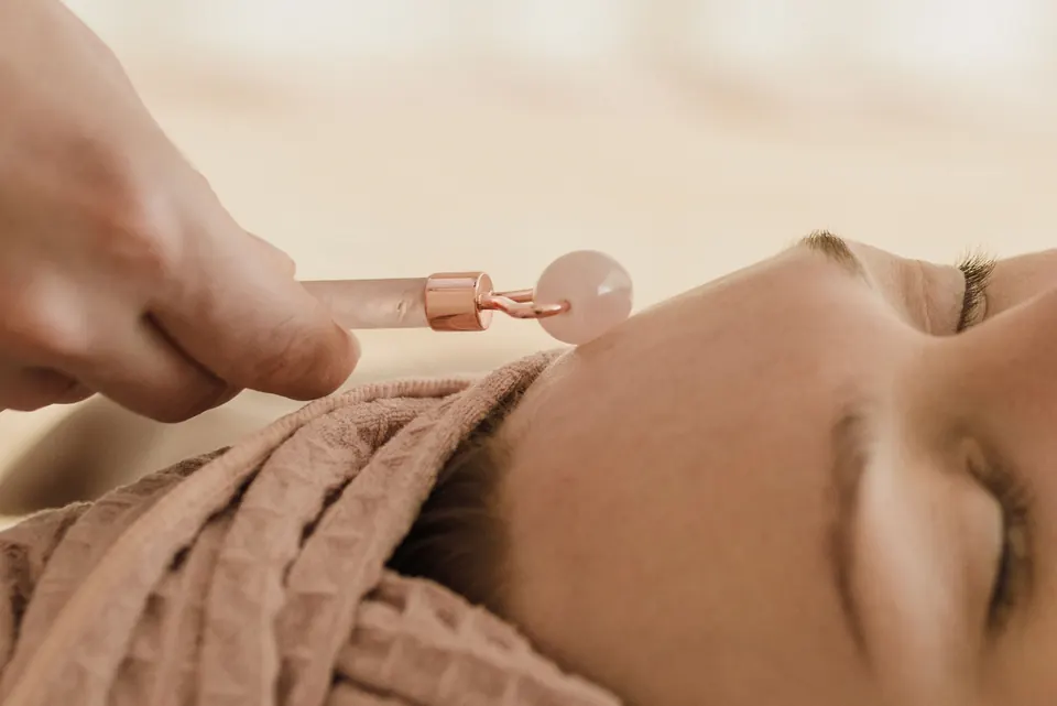 Un rodillo facial de cuarzo rosa sobre la mejilla de una mujer que descansa con una toalla