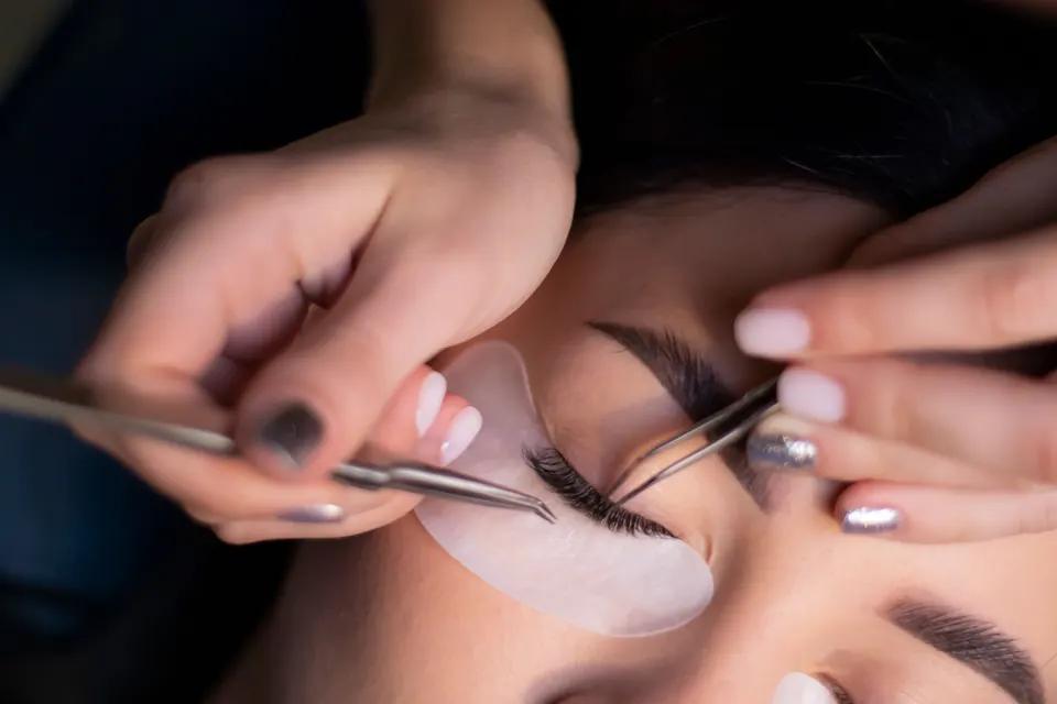 Una especialista pone extensiones de pestañas con pinzas