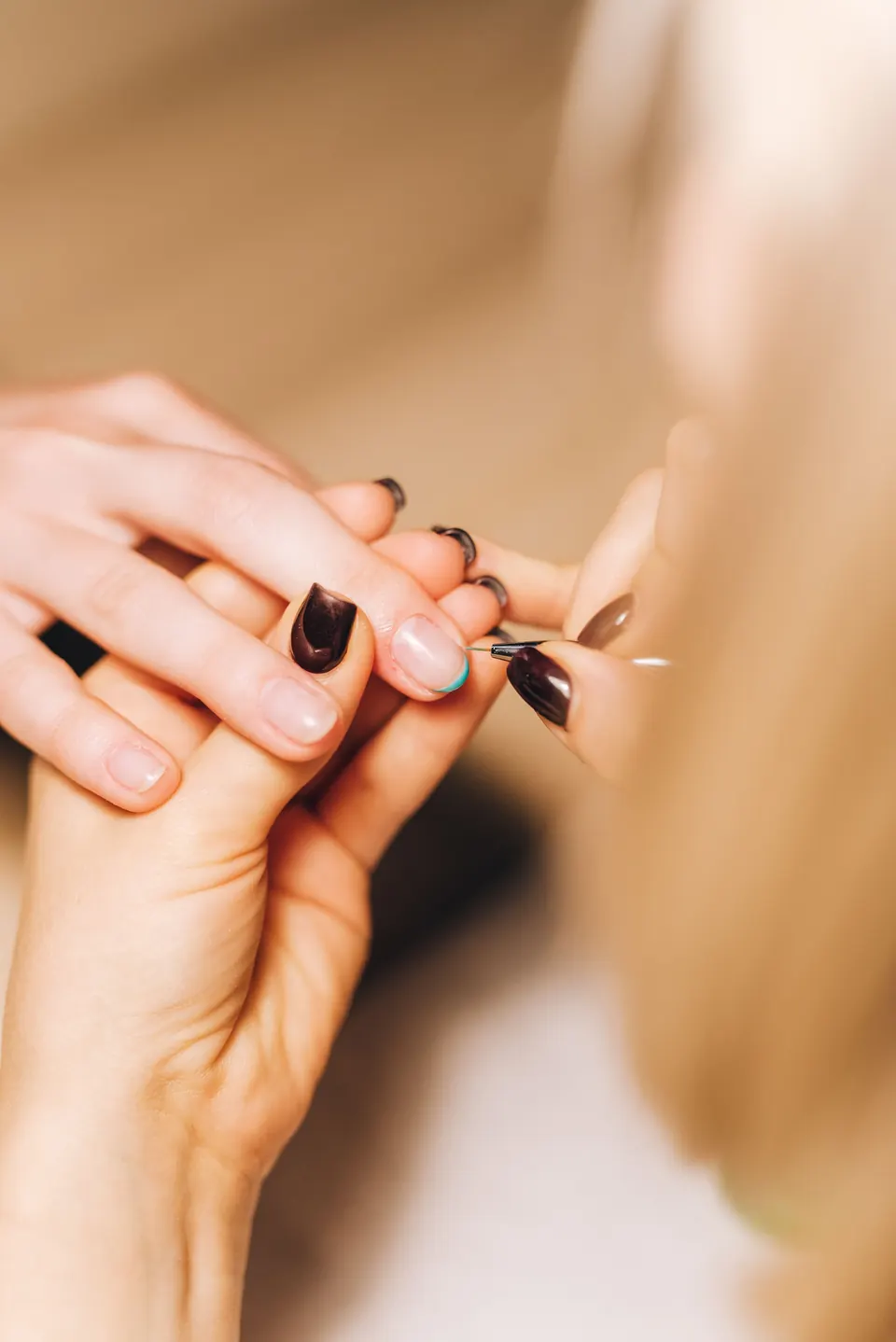 Manicura de cerca: una manicurista arregla las cutículas de unas uñas color vino